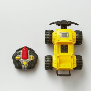 Overhead view of a yellow remote-controlled toy car with its controller on a white background.